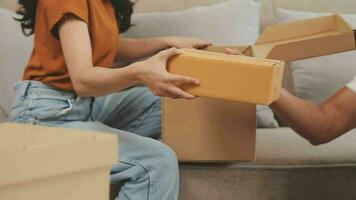 Moving to a new apartment. Happy newlyweds bought their first home, stand in the living room among the boxes, hold cardboard boxes in their hands, prepare to unpack things, look at the camera, smile video