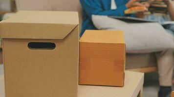 Moving to a new apartment. Happy newlyweds bought their first home, stand in the living room among the boxes, hold cardboard boxes in their hands, prepare to unpack things, look at the camera, smile video