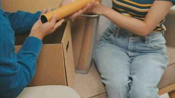 Moving to a new apartment. Happy newlyweds bought their first home, stand in the living room among the boxes, hold cardboard boxes in their hands, prepare to unpack things, look at the camera, smile video