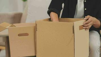 en mouvement à une Nouveau appartement. content jeunes mariés acheté leur premier maison, supporter dans le vivant pièce parmi le des boites, tenir papier carton des boites dans leur mains, préparer à déballer choses, Regardez à le caméra, sourire video