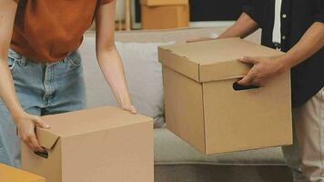 Moving to a new apartment. Happy newlyweds bought their first home, stand in the living room among the boxes, hold cardboard boxes in their hands, prepare to unpack things, look at the camera, smile video