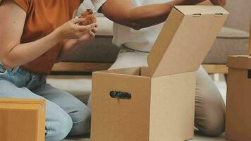 comovente para uma Novo apartamento. feliz recém-casados comprou seus primeiro lar, ficar de pé dentro a vivo quarto entre a caixas, aguarde cartão caixas dentro seus mãos, preparar para desempacotar coisas, Veja às a Câmera, sorrir video