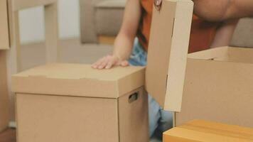 Moving to a new apartment. Happy newlyweds bought their first home, stand in the living room among the boxes, hold cardboard boxes in their hands, prepare to unpack things, look at the camera, smile video