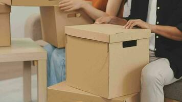 en mouvement à une Nouveau appartement. content jeunes mariés acheté leur premier maison, supporter dans le vivant pièce parmi le des boites, tenir papier carton des boites dans leur mains, préparer à déballer choses, Regardez à le caméra, sourire video