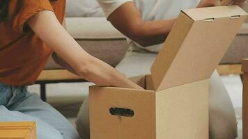 Moving to a new apartment. Happy newlyweds bought their first home, stand in the living room among the boxes, hold cardboard boxes in their hands, prepare to unpack things, look at the camera, smile video