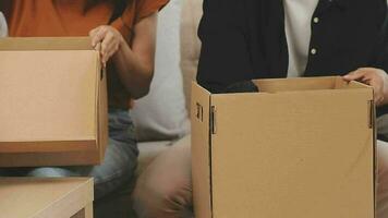 Moving to a new apartment. Happy newlyweds bought their first home, stand in the living room among the boxes, hold cardboard boxes in their hands, prepare to unpack things, look at the camera, smile video