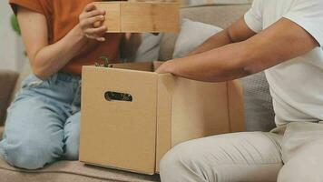 Moving to a new apartment. Happy newlyweds bought their first home, stand in the living room among the boxes, hold cardboard boxes in their hands, prepare to unpack things, look at the camera, smile video