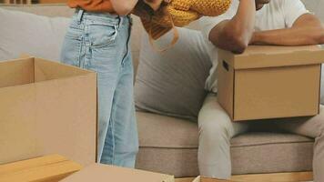 Moving to a new apartment. Happy newlyweds bought their first home, stand in the living room among the boxes, hold cardboard boxes in their hands, prepare to unpack things, look at the camera, smile video