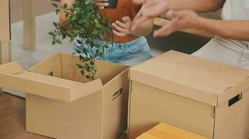 Moving to a new apartment. Happy newlyweds bought their first home, stand in the living room among the boxes, hold cardboard boxes in their hands, prepare to unpack things, look at the camera, smile video