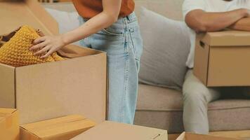 Moving to a new apartment. Happy newlyweds bought their first home, stand in the living room among the boxes, hold cardboard boxes in their hands, prepare to unpack things, look at the camera, smile video