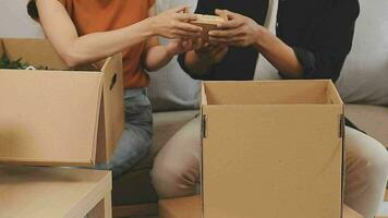 Moving to a new apartment. Happy newlyweds bought their first home, stand in the living room among the boxes, hold cardboard boxes in their hands, prepare to unpack things, look at the camera, smile video