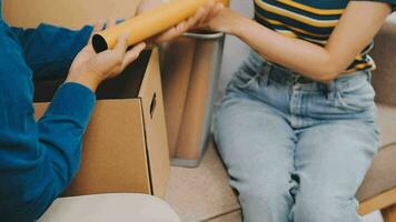 Two people couple interracial family ameste in living room in new apartment open cardboard boxes receive parcels with orders from internet store with new interior items rejoice at courier delivery video