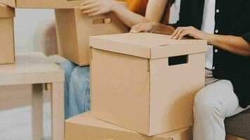 Two people couple interracial family ameste in living room in new apartment open cardboard boxes receive parcels with orders from internet store with new interior items rejoice at courier delivery video