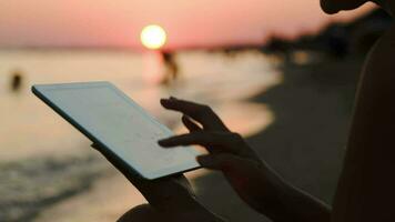 Mädchen Arbeiten mit Tablette pc auf Strand beim Sonnenuntergang, Handheld Schuss video