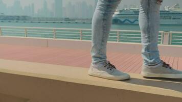 une Jeune homme dans jeans, baskets et une blanc T-shirt des promenades le long de le parapet le long de le digue. lent mouvement video