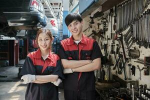 Portrait of two professional Asian mechanic partners smile and arms crossed with hand tools machinery, fixing work at car service garage, maintenance and repair jobs in automotive industry business. photo