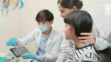 Asian male pediatric dentist explains teeth X-ray scan to girl and her mother for dentistry hygiene from tablet in dental clinic, professional orthodontic oral doctor in a kid healthcare hospital. video