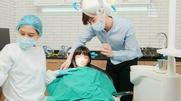 Asian female pediatric dentist checks and examines girl's teeth with her father encouraged in dental clinic, well-being hygiene, and professional orthodontic healthcare doctor in children hospital. video