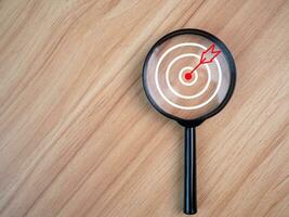 Magnifying glass with target icon placed on wooden table background. Business concept. Management concept. Business planning concept. business goal setting concept photo