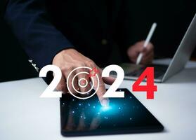 Businessman pointing at tablet showing dartboard icon with numbers Represents goal setting for 2024. Startup concept, financial planning, development strategy, business goal setting, photo