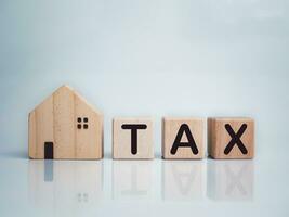 Model wooden house and wooden blocks with the letters TAX printed on them. Real estate tax. Tax collection on the purchase or sale of a home, tax interest, investment returns. tax deduction photo