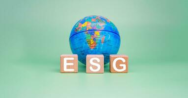 ESG concept for environment, society and governance in sustainable. business responsible environmental. Wooden blocks with ESG letters printed on them and a model of the earth on a green background. photo