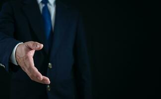 Businessman standing and doing handshake gesture on dark background. Business concept. Copy space. photo