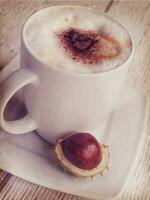 hot autumn coffee with foam and chestnuts on a wooden background photo