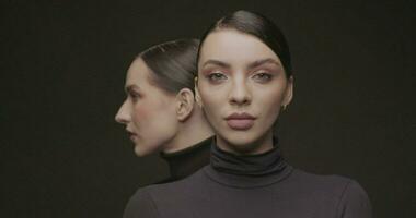 dos joven elegante mujer con bueno maquillaje en un negro antecedentes. lento movimiento, estudio disparo. video