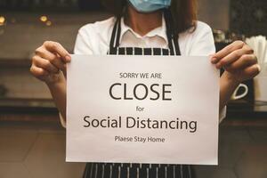 young woman wearing a mask running a coffee shop business Hold a white paper banner with a message of closing the shop and social distancing. Entrepreneurs Doing Business During the Coronavirus Spread photo