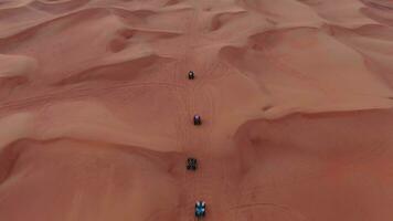 A drone flies over quad bikes driving through the sand dunes of the desert in the United Arab Emirates. Aerial view video