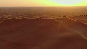 A drone flies over ATVs standing on the sand dunes of the desert against the backdrop of the sunset. Aerial view video
