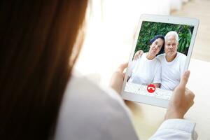 The concept of connecting with communication through online technology. A female doctor with a tablet Chat online, treat Asian elderly patients through video calls. photo