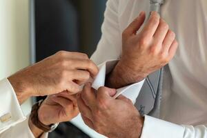 groom getting ready for his wedding and putting on his cufflinks photo