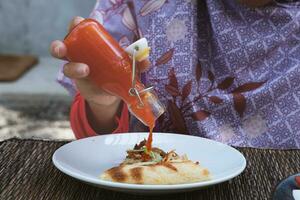 A hijab-wearing woman pours sauce on a slice of pizza served on a white plate. photo