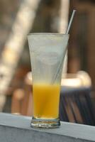 Orange squash is served in a glass with a straw made of stainless steel. You can see small bubbles from the soda water photo