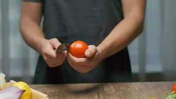 une professionnel chef coupes une tomate tandis que en portant il. proche en haut lent mouvement. video