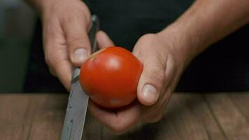 un' professionale capocuoco tagli un' pomodoro mentre Tenere esso. vicino su lento movimento. video