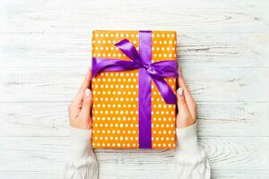 Female's hands holding striped gift box with colored ribbon on white rustic wooden background. Christmas concept or other holiday handmade present box, concept top view with copy space photo