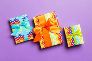 wrapped Christmas or other holiday handmade present in paper with blue, green and orange ribbon on purple background. Present box, decoration of gift on colored table, top view photo