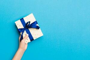 Woman arms holding gift box with colored ribbon on blue table background, top view and copy space for you design photo