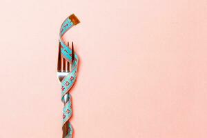 Close up of fork wrapped in measuring tape on pink background. Overweight and overeating concept photo