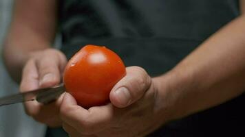 une professionnel chef coupes une tomate tandis que en portant il. proche en haut lent mouvement. video