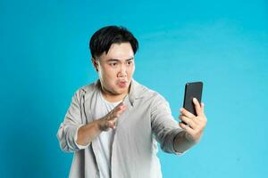 Image of Asian man using phone on blue background photo