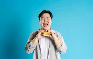 retrato de asiático hombre comiendo rápido comida en azul antecedentes foto