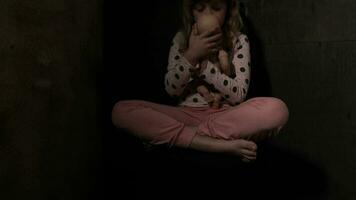 uma jovem menina sentado em a chão com dela boneca dentro a Sombrio video