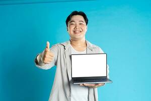 Image of Asian man using laptop on blue background photo