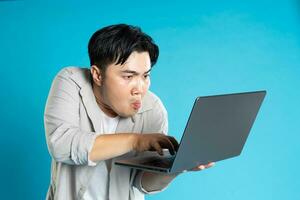 Image of Asian man using laptop on blue background photo
