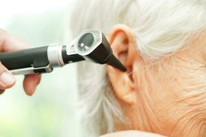 Otolaryngologist or ENT physician doctor examining senior patient ear with otoscope, hearing loss problem. photo