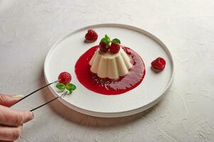 Woman's hand puts tweezers leaf mint to panna cotta with syrup, raspberries and mint photo